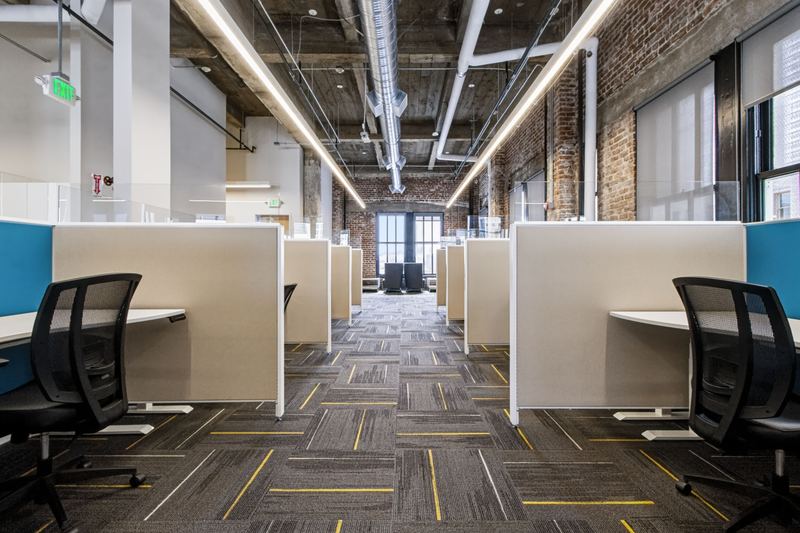 Workstations on an open floor with brick walls and tall windows